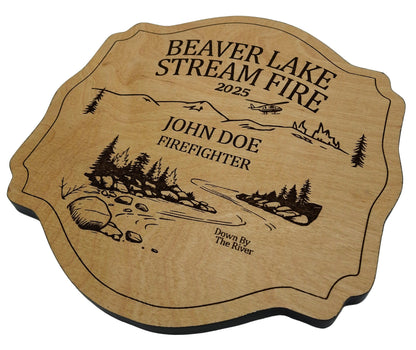 Wooden fire plaque with engraved design of a forest and text, on a light gray background